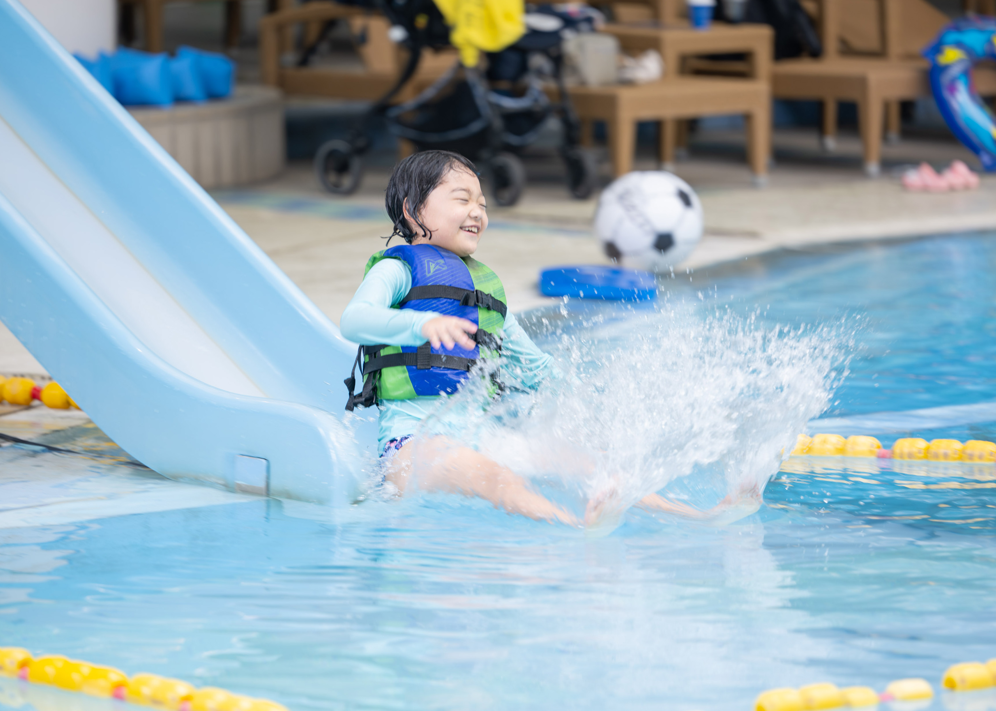 ライフジャケットを着用してプールのすべり台で遊ぶ子ども